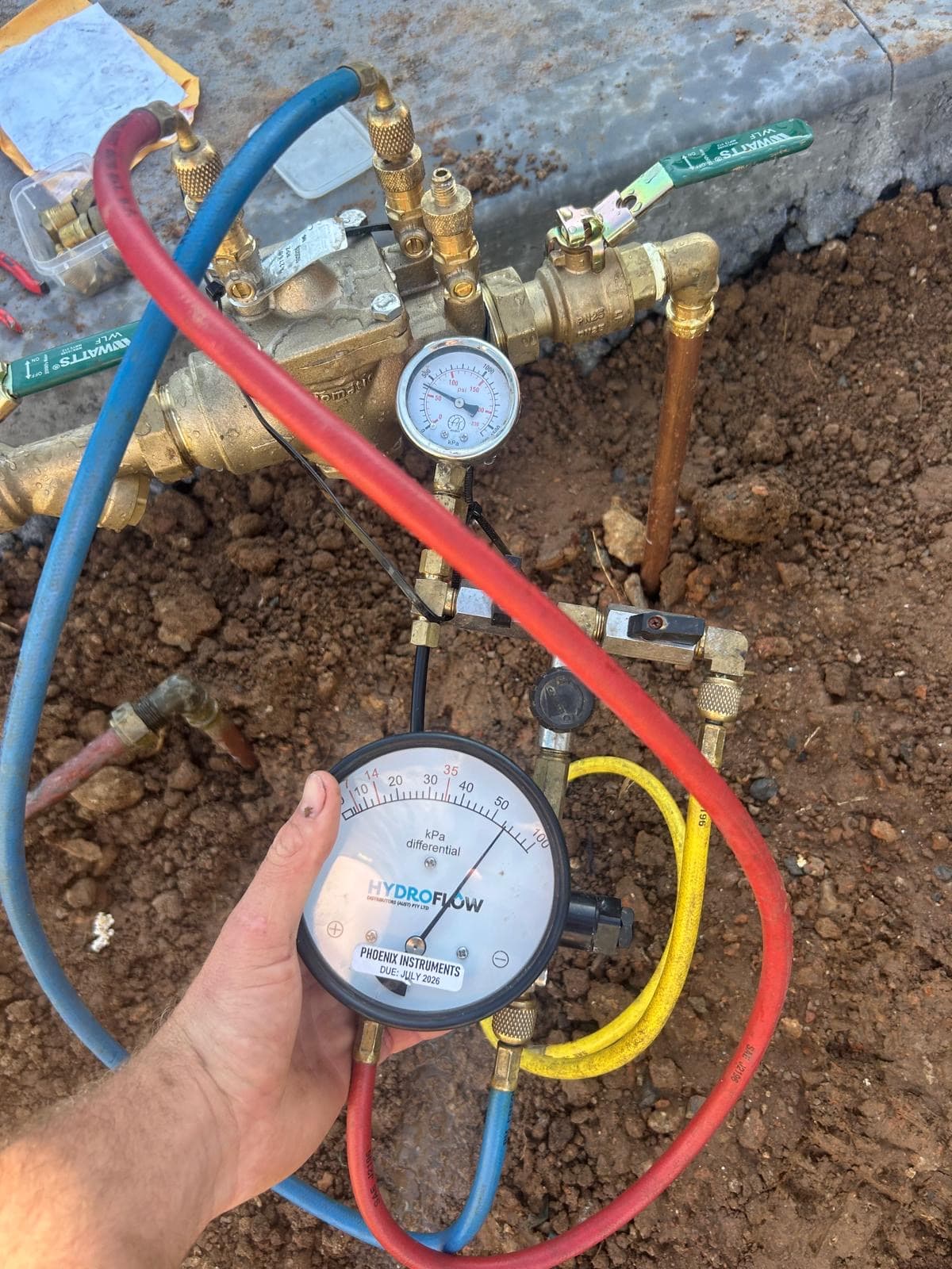 Backflow test by TBH Plumbing Solutions: gauge and test hoses connected to a backflow device in a trench